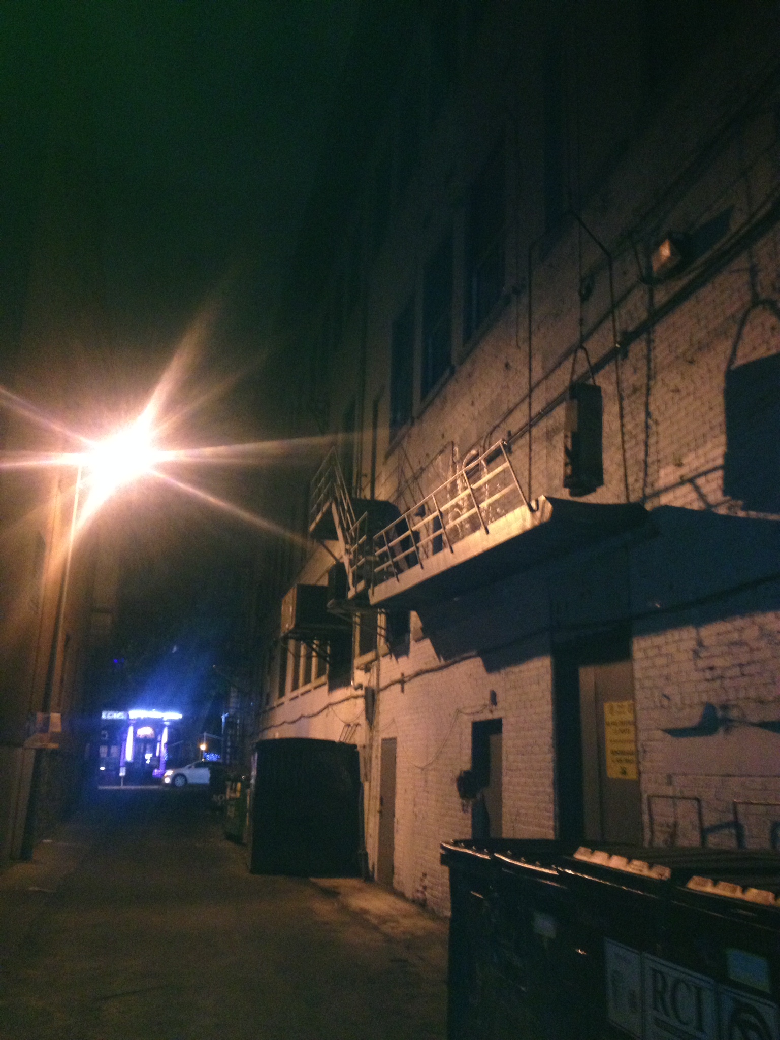 Night alley beside an industrial brick building, cut by a glaring security light